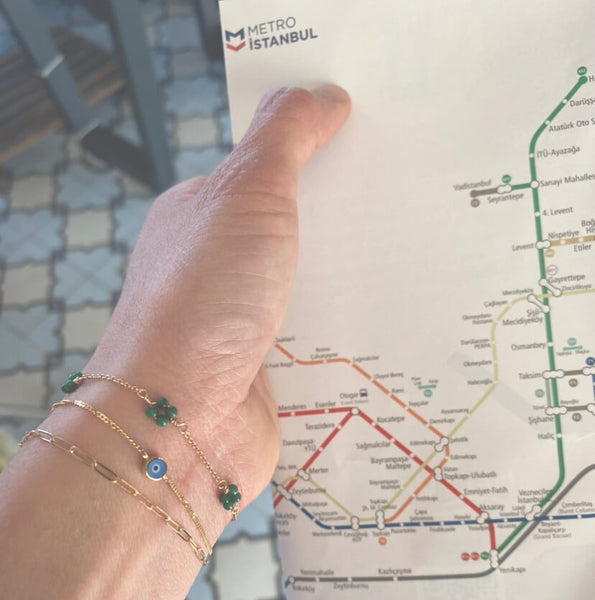 This is a dainty evil eye bracelet that's made of 14k solid gold. The hand is holding a metro map of Istanbul. 