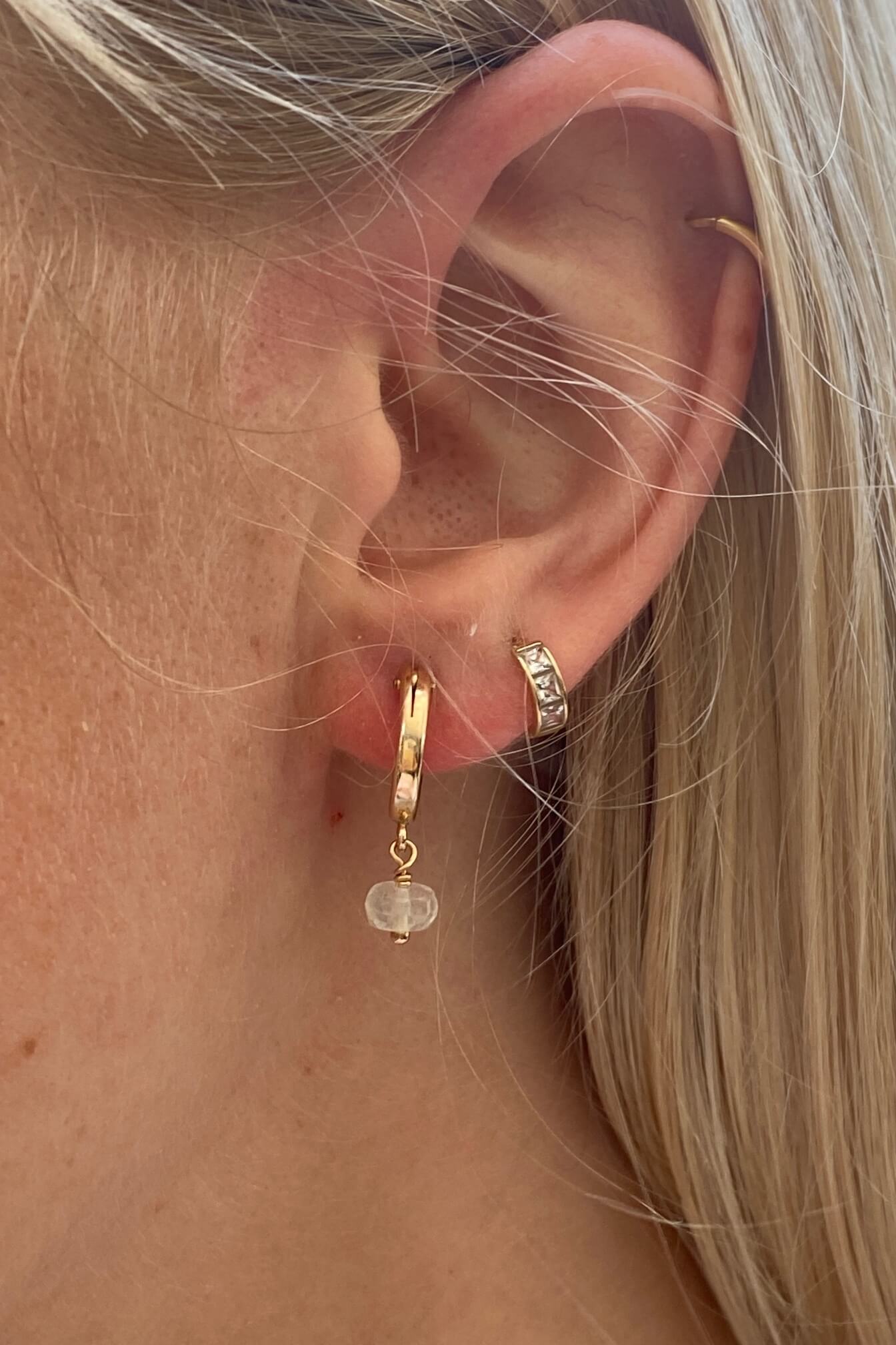 Gold Libyan desert glass earrings on a model layering it with another gold hoop earrings. 