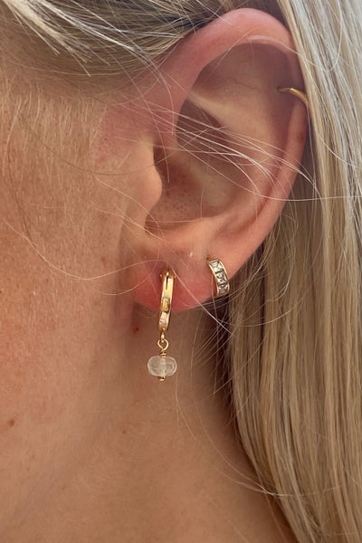 Gold Libyan desert glass earrings on a model layering it with another gold hoop earrings. 