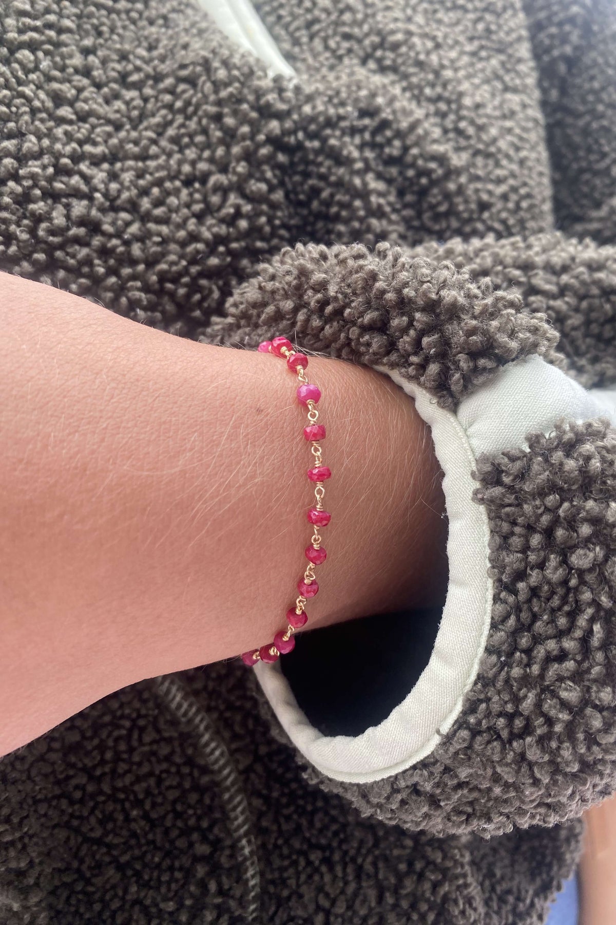 A close-up of a ruby bracelet made of ruby bead links, shown against a gray fleece jacket.