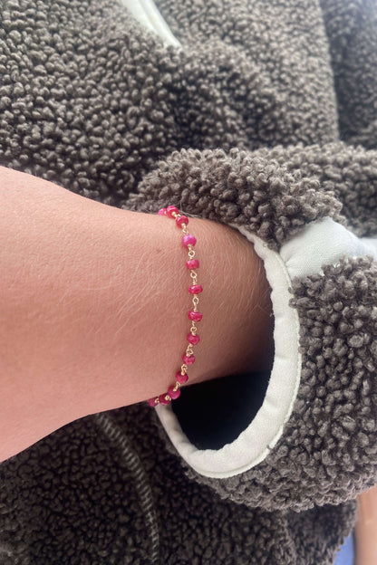 A close-up of a ruby bracelet made of ruby bead links, shown against a gray fleece jacket.